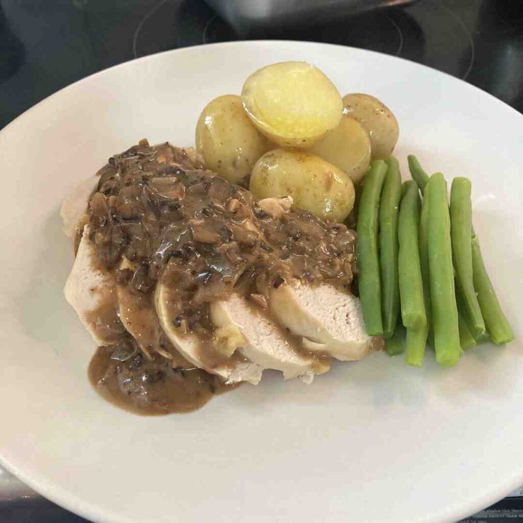 Sliced chicken breast with a mushroom sauce, green beans and new potatoes arranged artfully on a plate