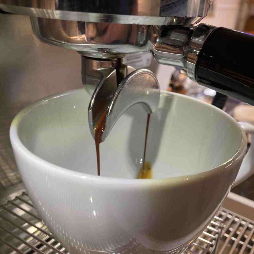 Freshly brewed coffee pouring from an espresso machine into a coffee cup
