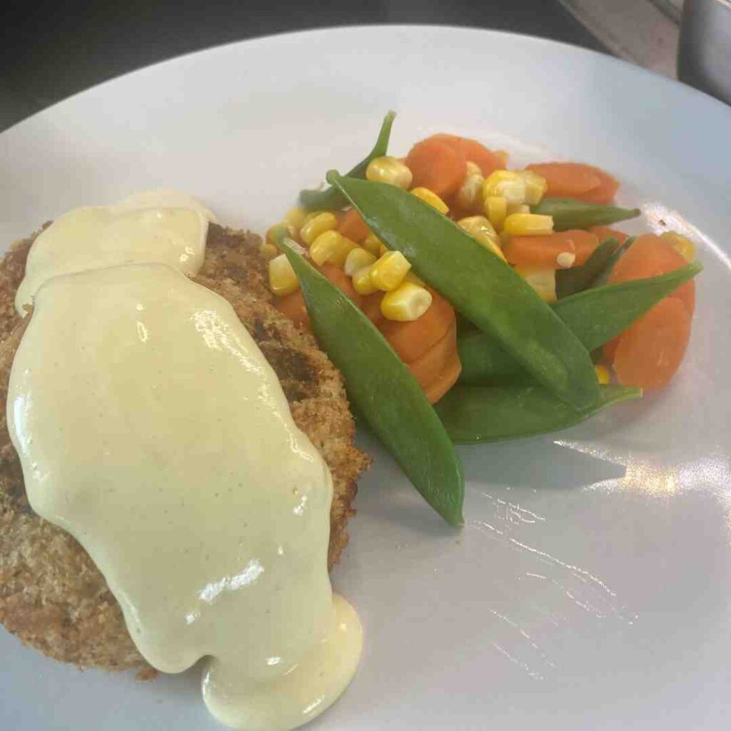 Fishcakes and tartare sauce with carrots, sweetcorn and mange tout, all artfully arranged on a plate