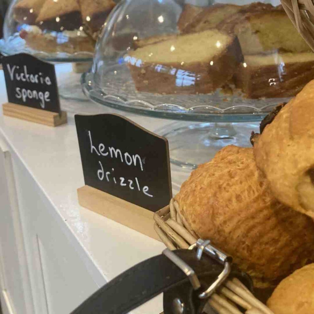 Café display of Victoria sponge and lemon drizzle cakes under glass domes and a basket of scones